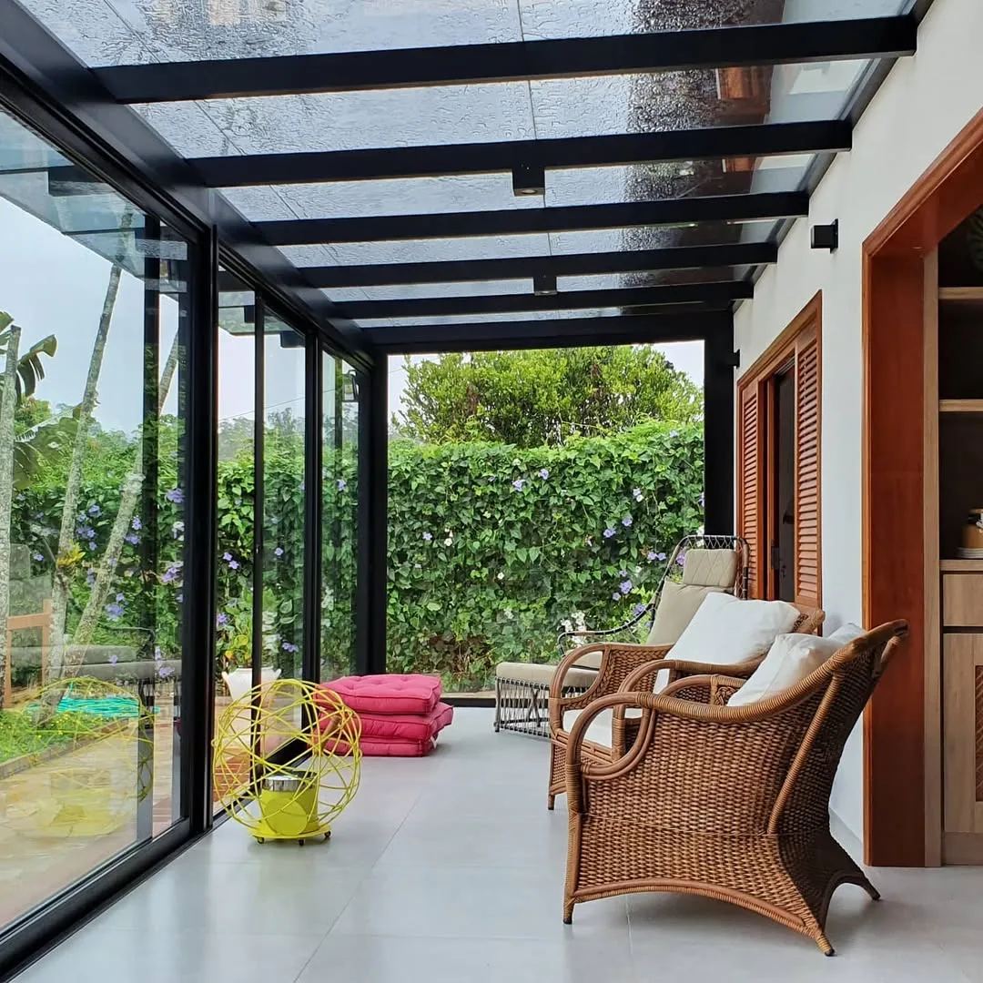 Pergolado de alumínio preto na varanda com poltronas confortáveis.