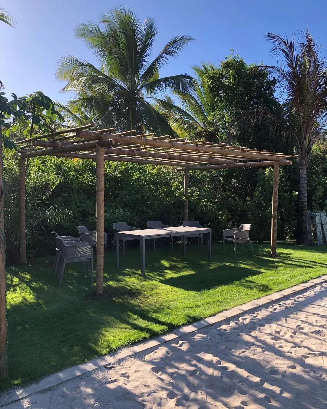 Pergolado de bambu, areia no chão e grama.