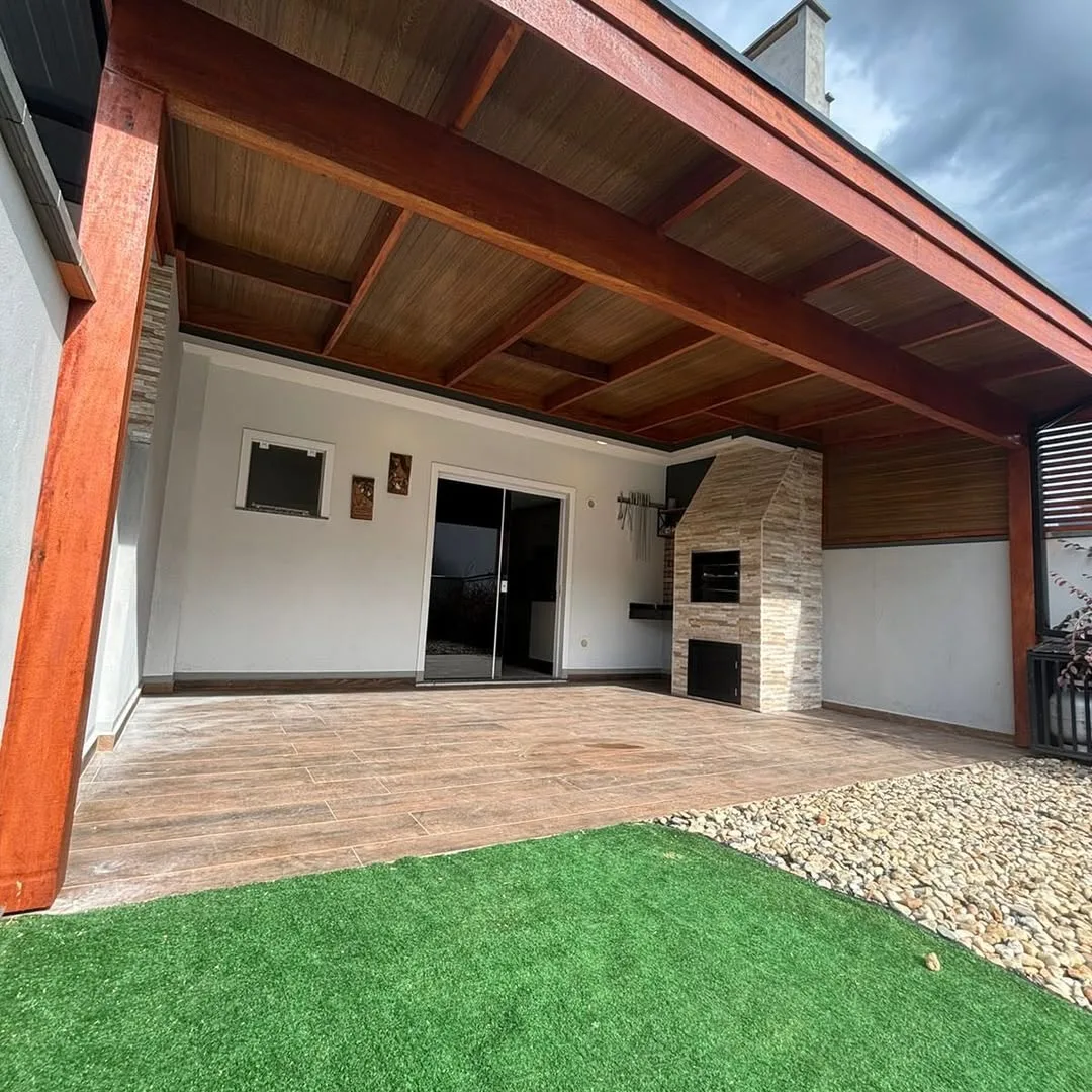 Pergolado na garagem feito de madeira e forrado, grama e piso no chão.