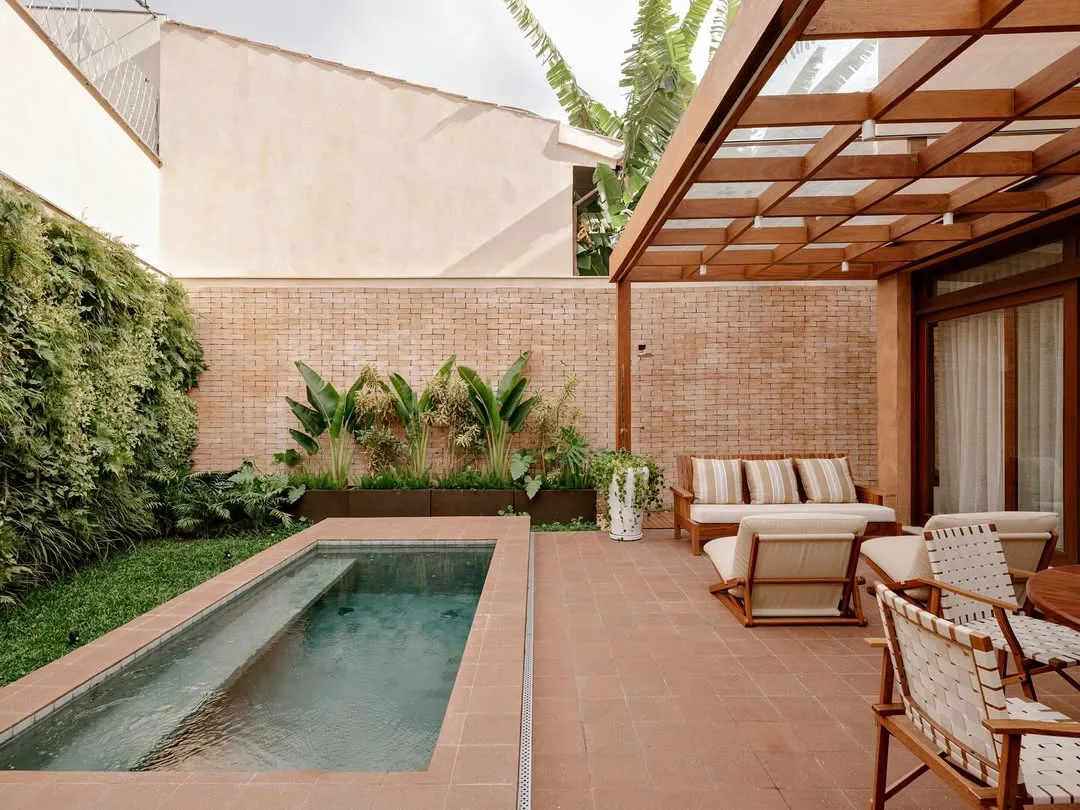 Pergolado comprido na área da piscina e feito de madeira com cobertura transparente.