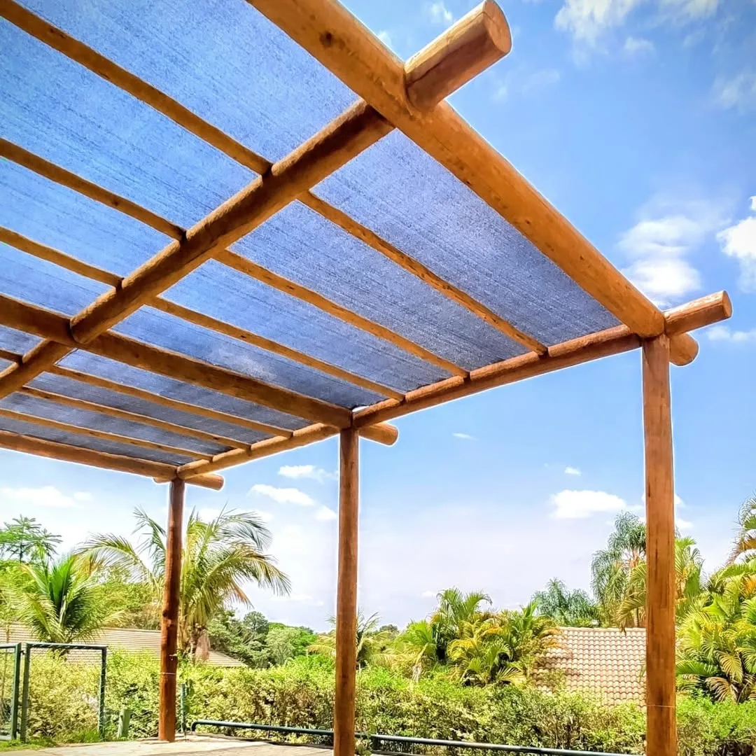 Pergolado de eucalipto com forro simples e paisagem de plantas ao fundo.