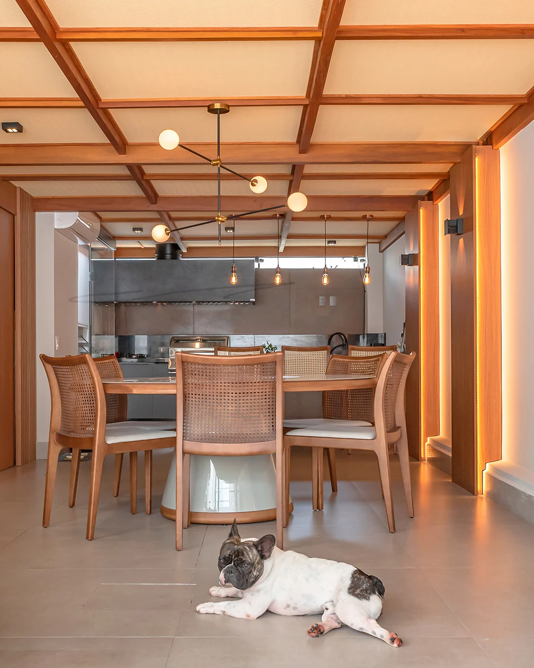 Pergolado na sala de jantar feito de madeira e forrado, cachorro no centro da imagem e cadeiras.