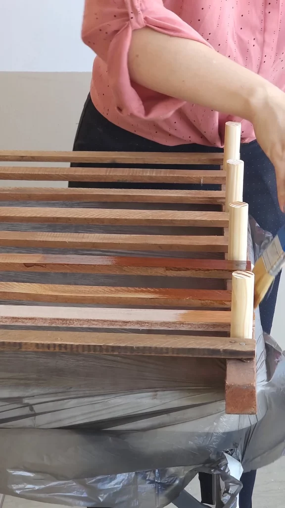 Passando verniz no estrado de cama com tocos de madeira pregados.