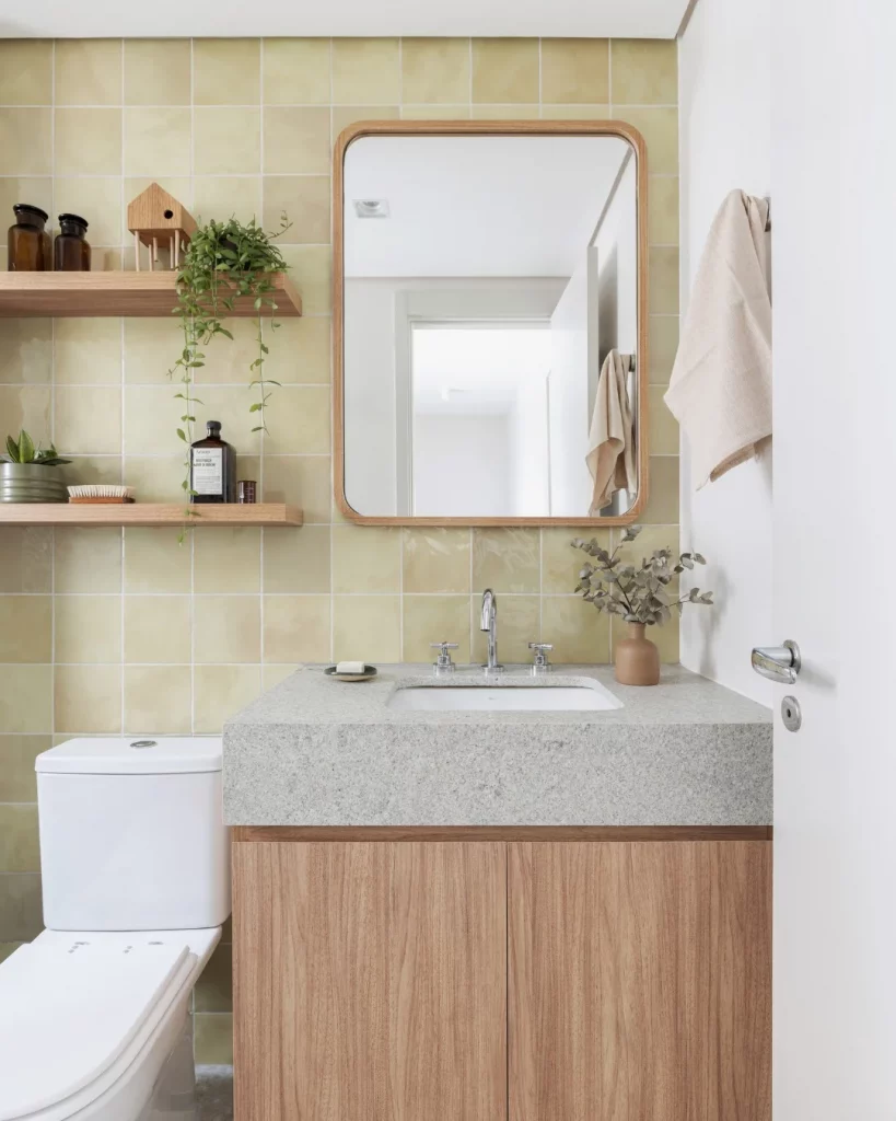 Prateleira de madeira com espelho ao lado, vaso sanitário branco e armário de madeira.