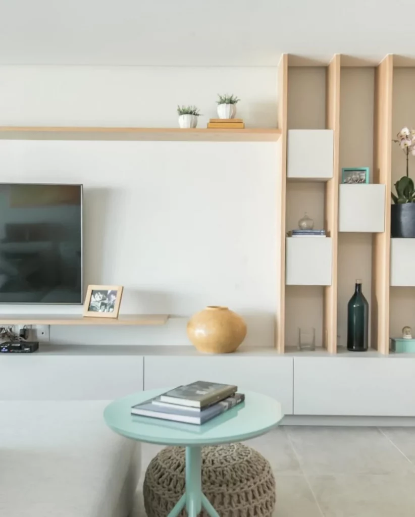 Prateleira de madeira clara, mesa de centro ao lado e televisão.