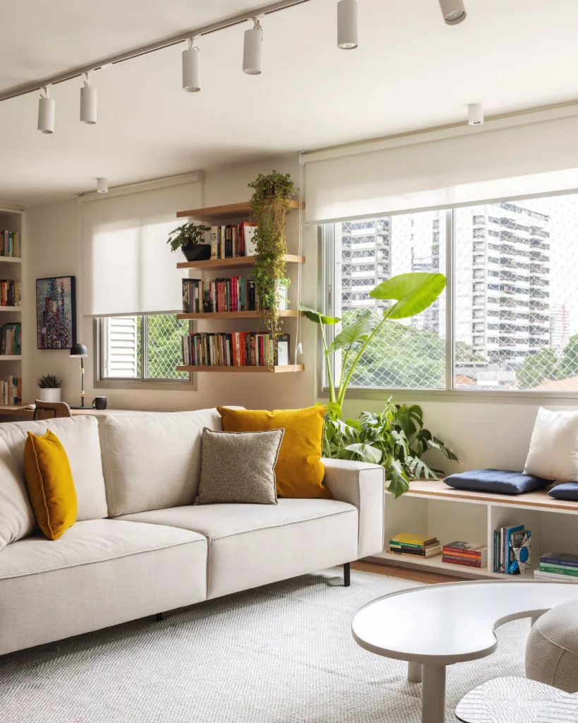 Prateleira de madeira com livros, sofá branco e almofadas coloridas.