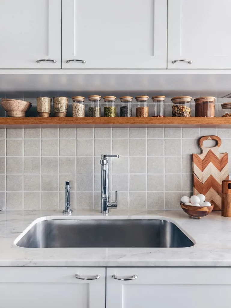 Prateleira na cozinha com armário acima, temperos organizados em linha reta.