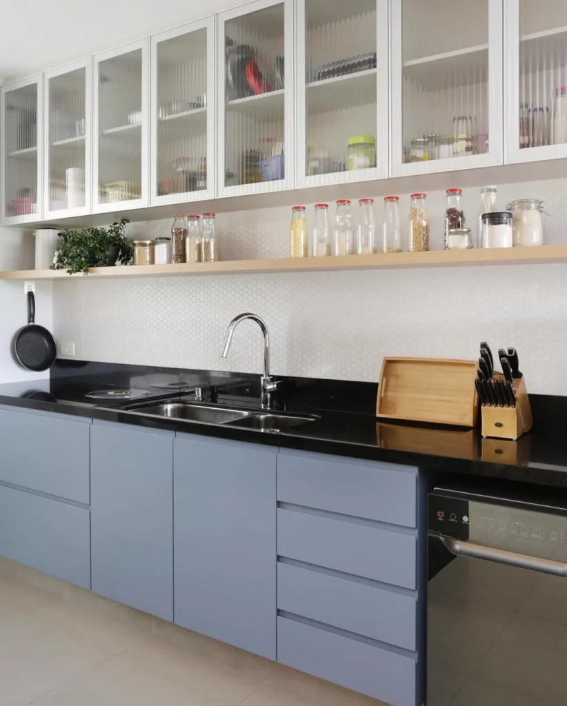 Prateleira de madeira na cozinha com temperos e armários azuis.