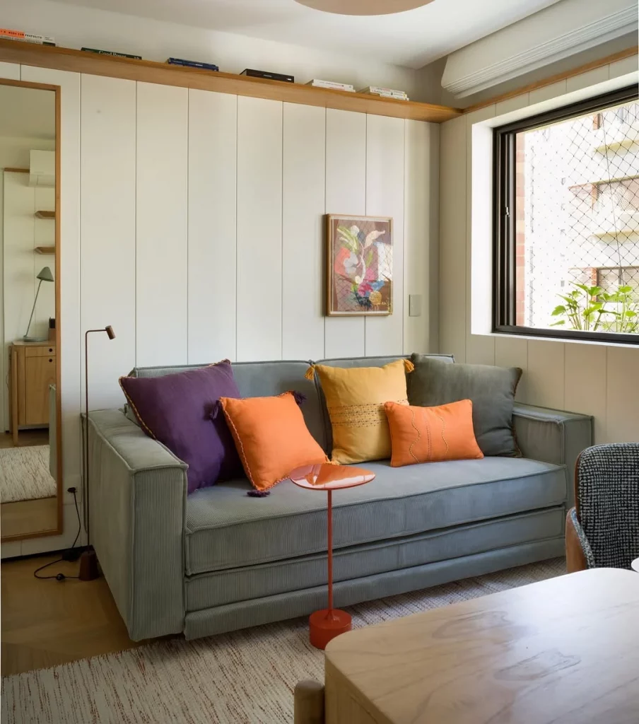 Prateleira de madeira na sala de estar com sofá cinza e almofadas coloridas.