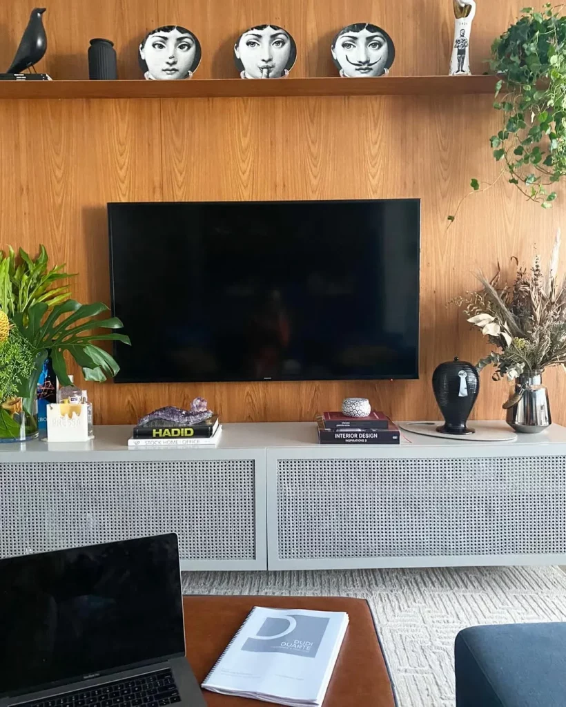 Prateleira de madeira na sala de televisão com painel no fundo e pratos decorativos em cima.