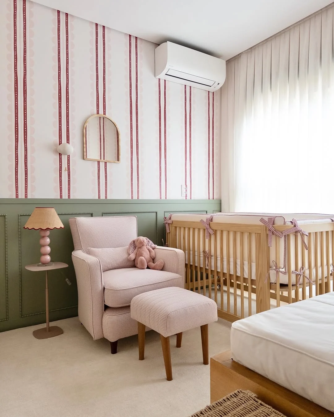 Quarto de bebê menina, parede listrada com vermelho e boiserie verde, berço de madeira.