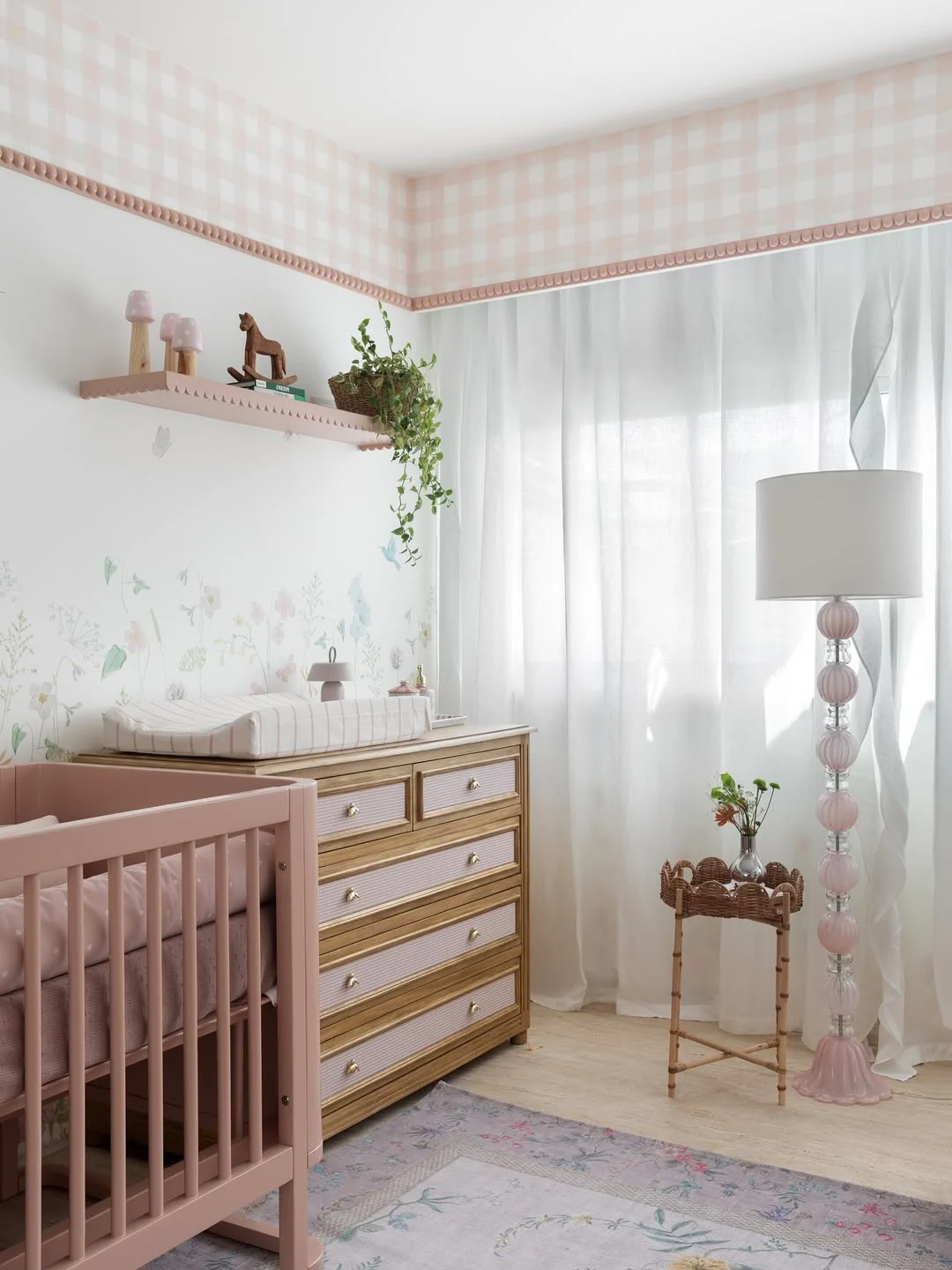 Cômoda de bebê rosa com madeira, berço rosa e abajur detalhado.