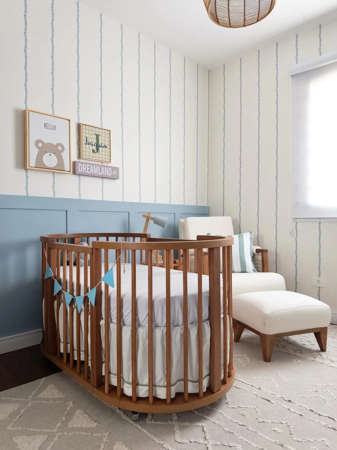 Quarto de menino com berço de madeira, parede listrada e poltrona de amamentação.