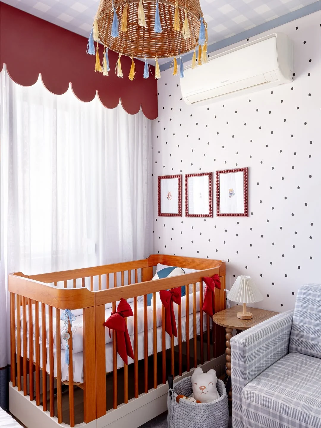 Quarto de bebê com berço de madeira, detalhes em vermelho e papel de parede de bolinha.