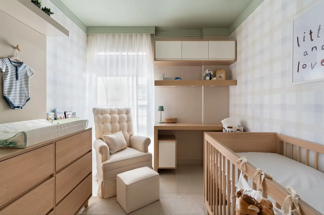 Quarto de bebê com janela ao fundo, armário suspenso, poltrona bege e berço de madeira.