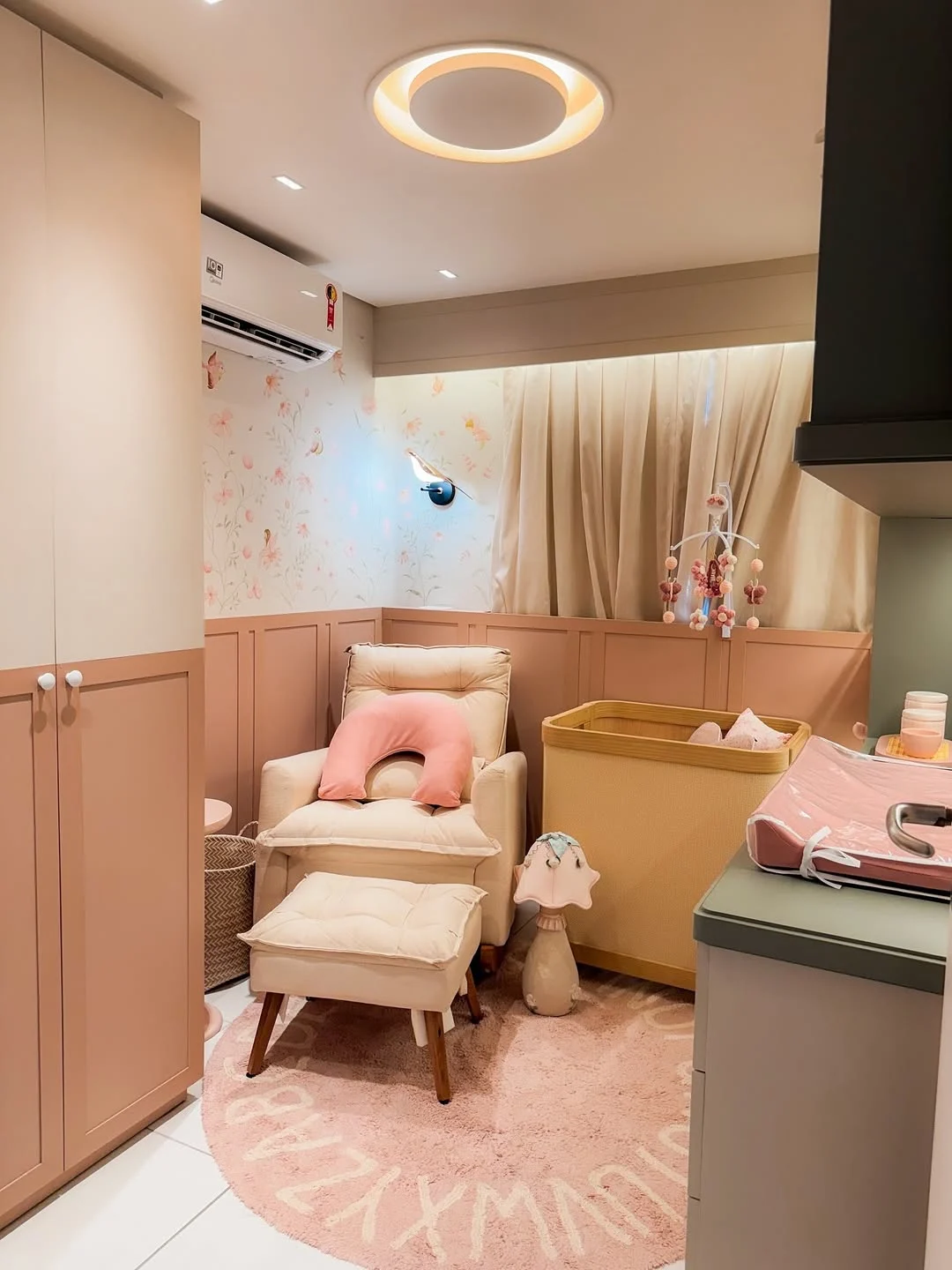 Quarto de bebê com boiserie rosé, poltrona de amamentação e berço.