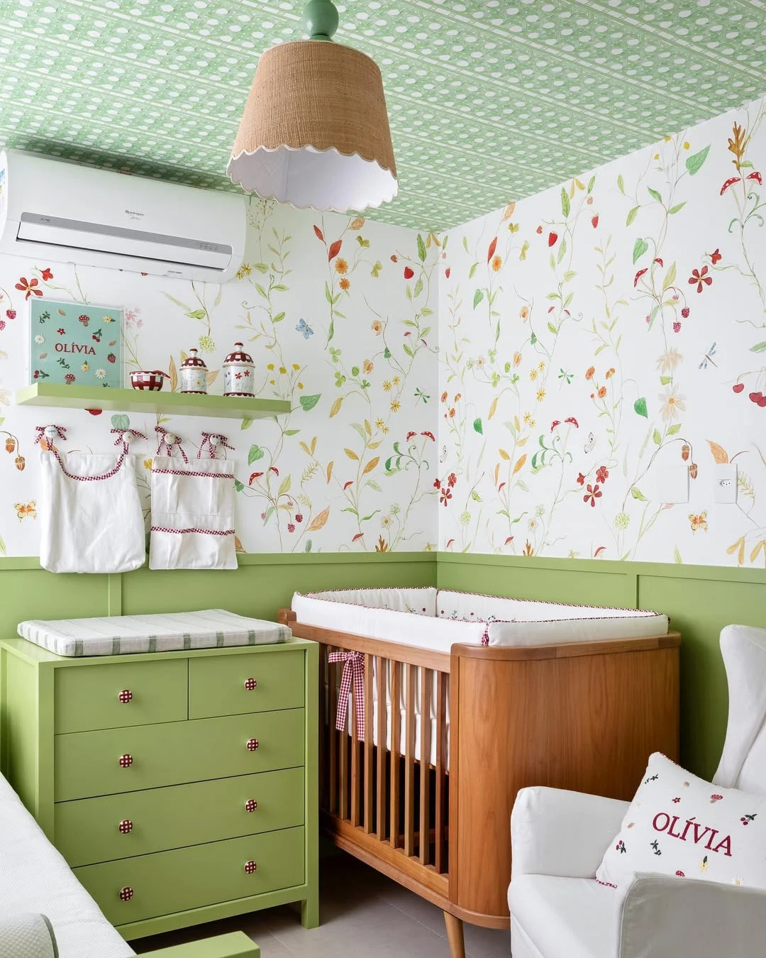 Quarto de bebê com berço de madeira, parede com detalhes verde e cômoda verde.