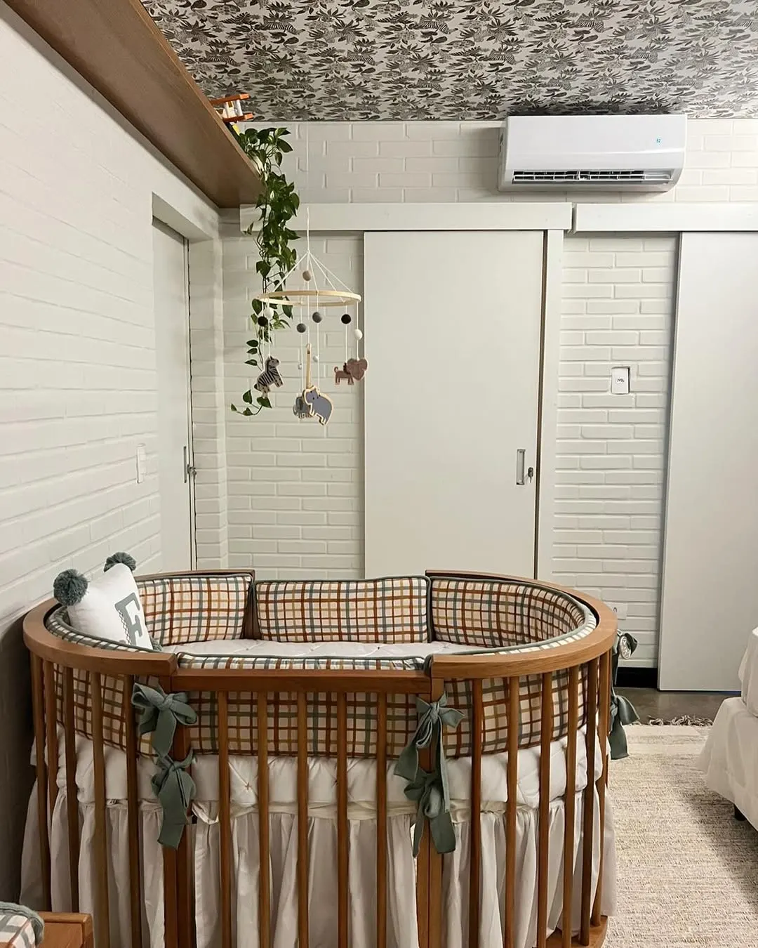 Quarto de bebê com planta, paredes de tijolinho e berço de madeira.