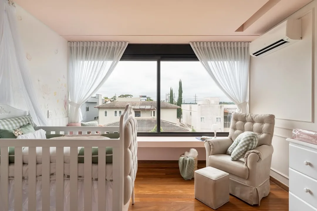 Quarto de bebê com janelas grandes de vidro, poltrona de amamentação e berço branco.
