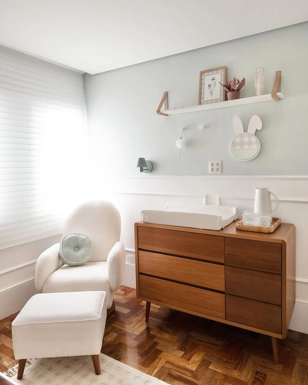 Quarto de bebê neutro com cômoda de madeira e prateleira na parede.