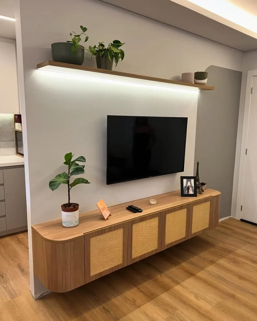 Móvel com palha indiana, cantos arredondados, de madeira, com prateleira iluminada acima e planta. 