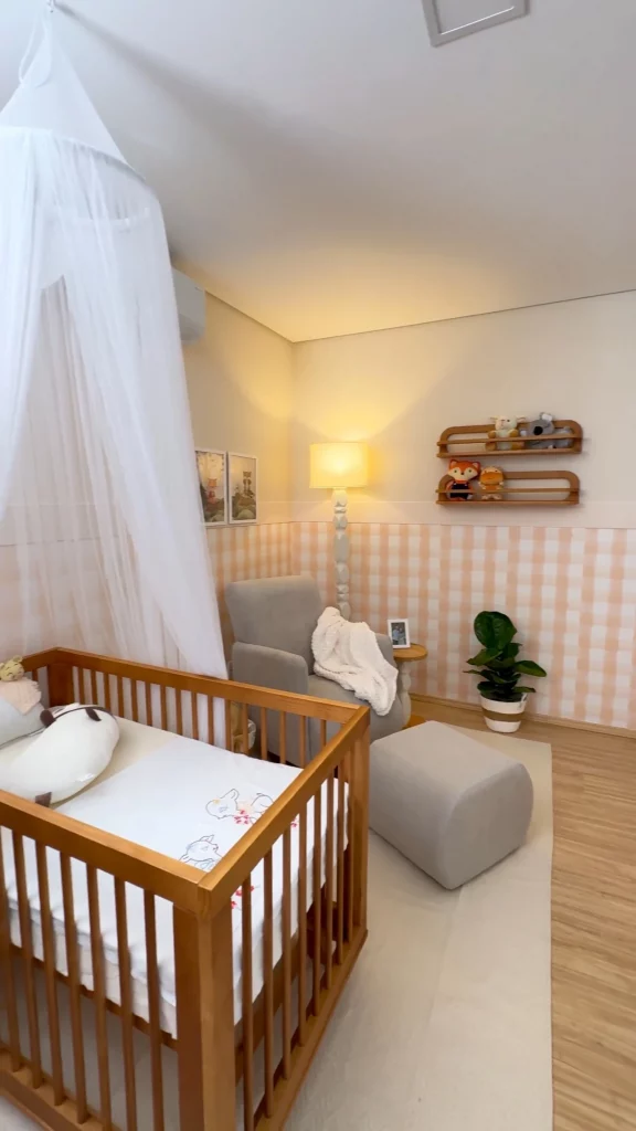 Resultado final do quarto de bebê, com quadros na parede xadrez, poltrona de amamentação, berço, guarda-roupas branco e tapete.