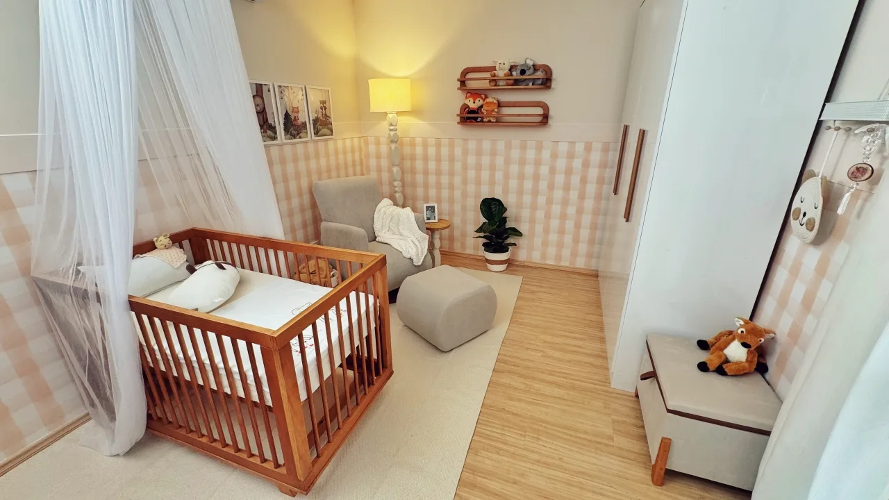 Resultado final do quarto de bebê, com quadros na parede xadrez, poltrona de amamentação, berço, guarda-roupas branco e tapete.