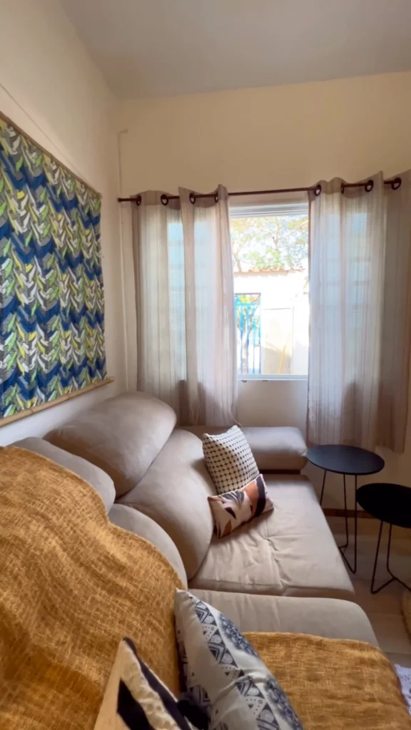 Sofá na parede oposta da porta, tecido na parede, manta e mesas pretas no canto.