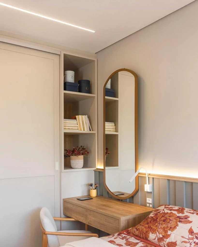 Penteadeira ao lado da cama com espelho oval com moldura de madeira.