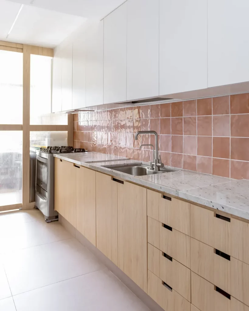 Cozinha com armário de madeira e azulejo rosa.