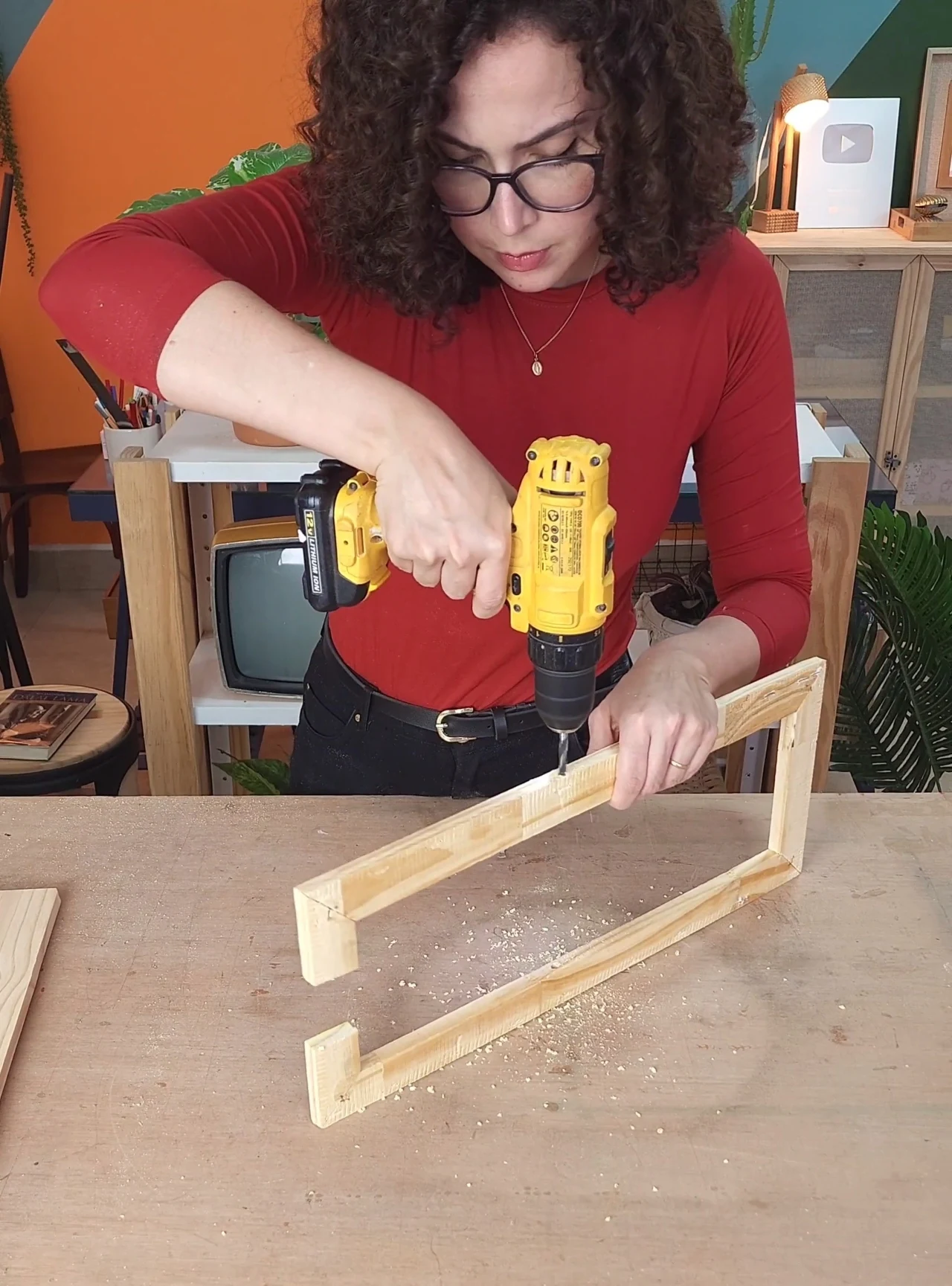 Fazendo furo com furadeira na lateral da moldura de madeira clara da mesa.