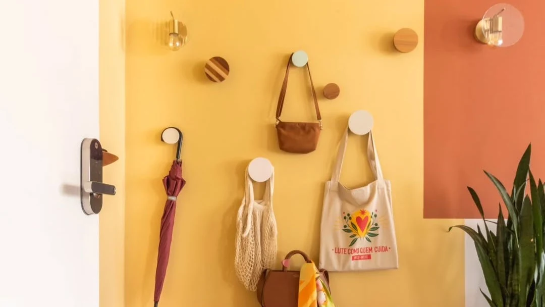 Parede amarela e terracota com ganchos e acessórios pendurados.