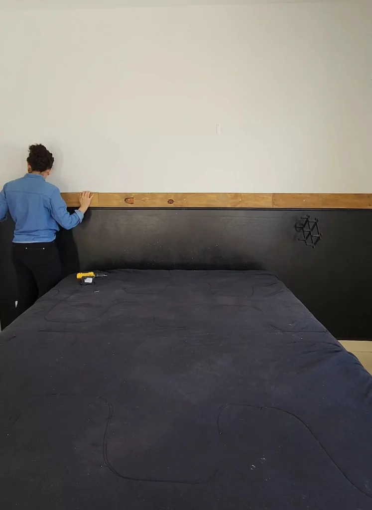 Instalando prateleira de madeira no quarto com parede preta.