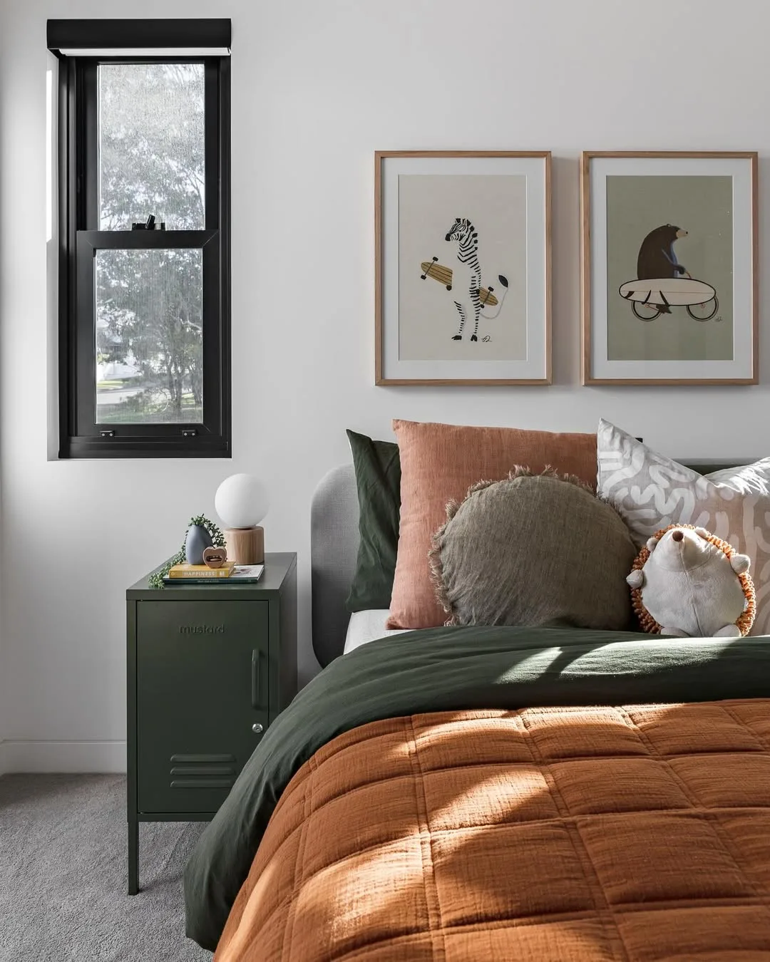 Cama com almofadas de tamanhos e formas diferentes, parede branca com quadros de bichos.