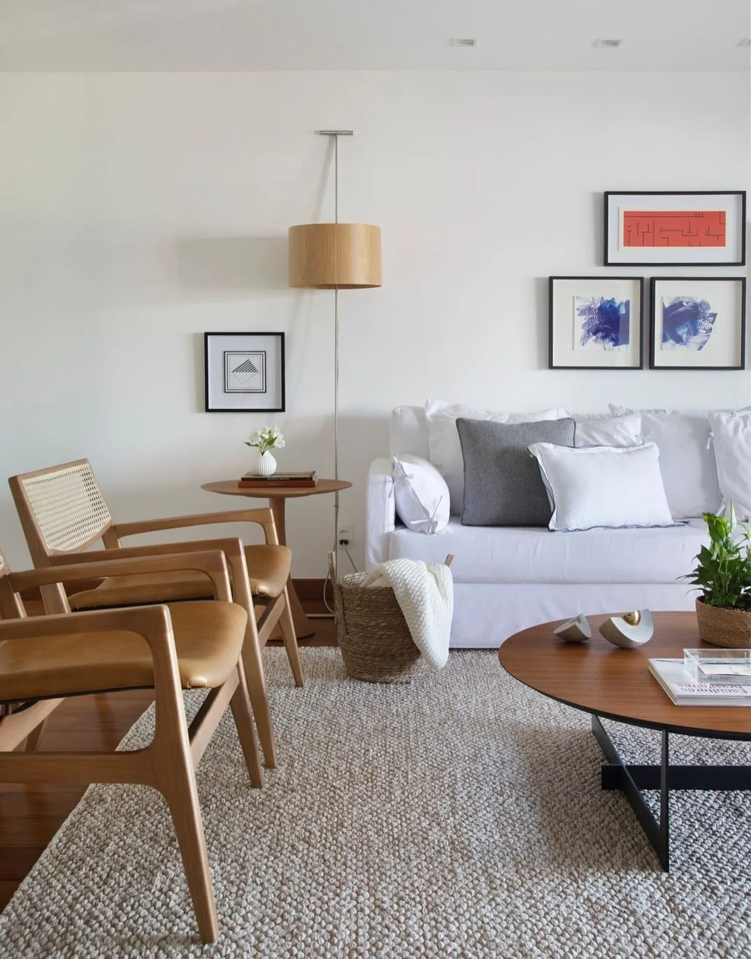 Sala de estar com sofá cinza claro, almofadas, quadros na parede, poltrona de madeira e couro.