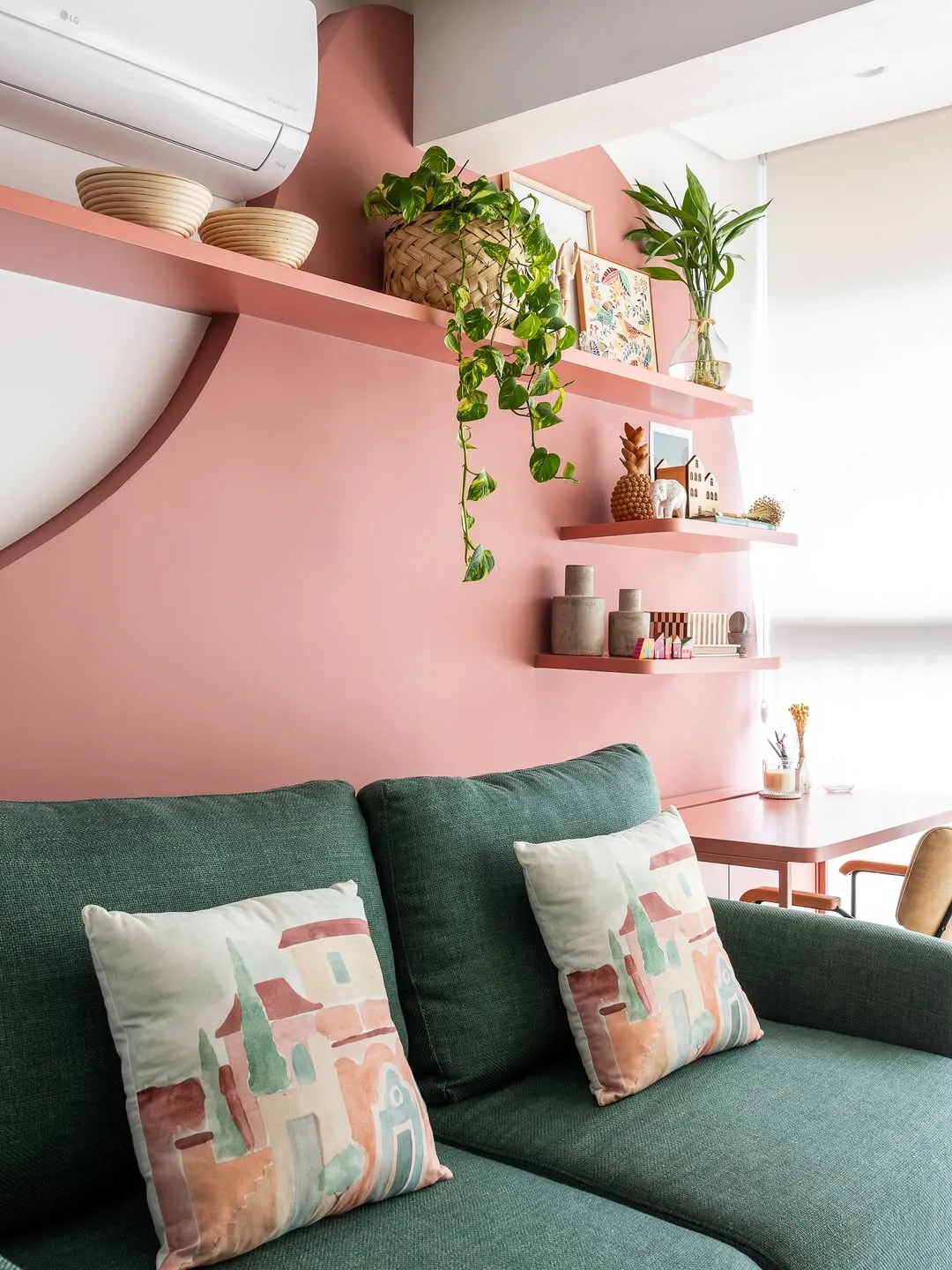 Sofá e home office compartilhados, parede rosa e almofada estampada de casa.