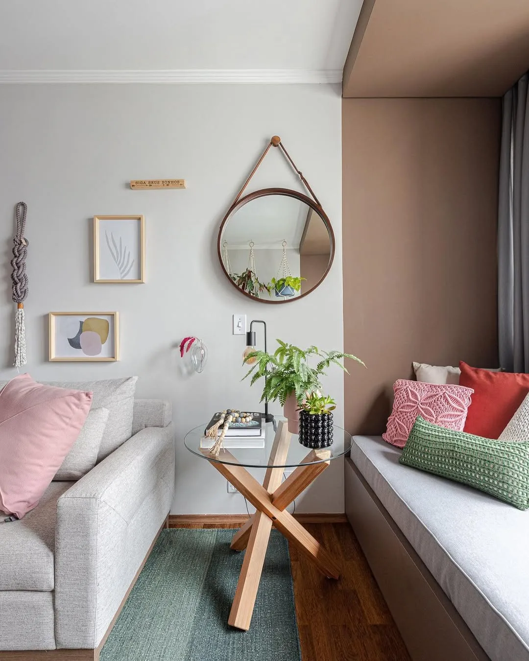 Almofadas coloridas no sofá e no cantinho ad parede, espelho redondo pendurado.