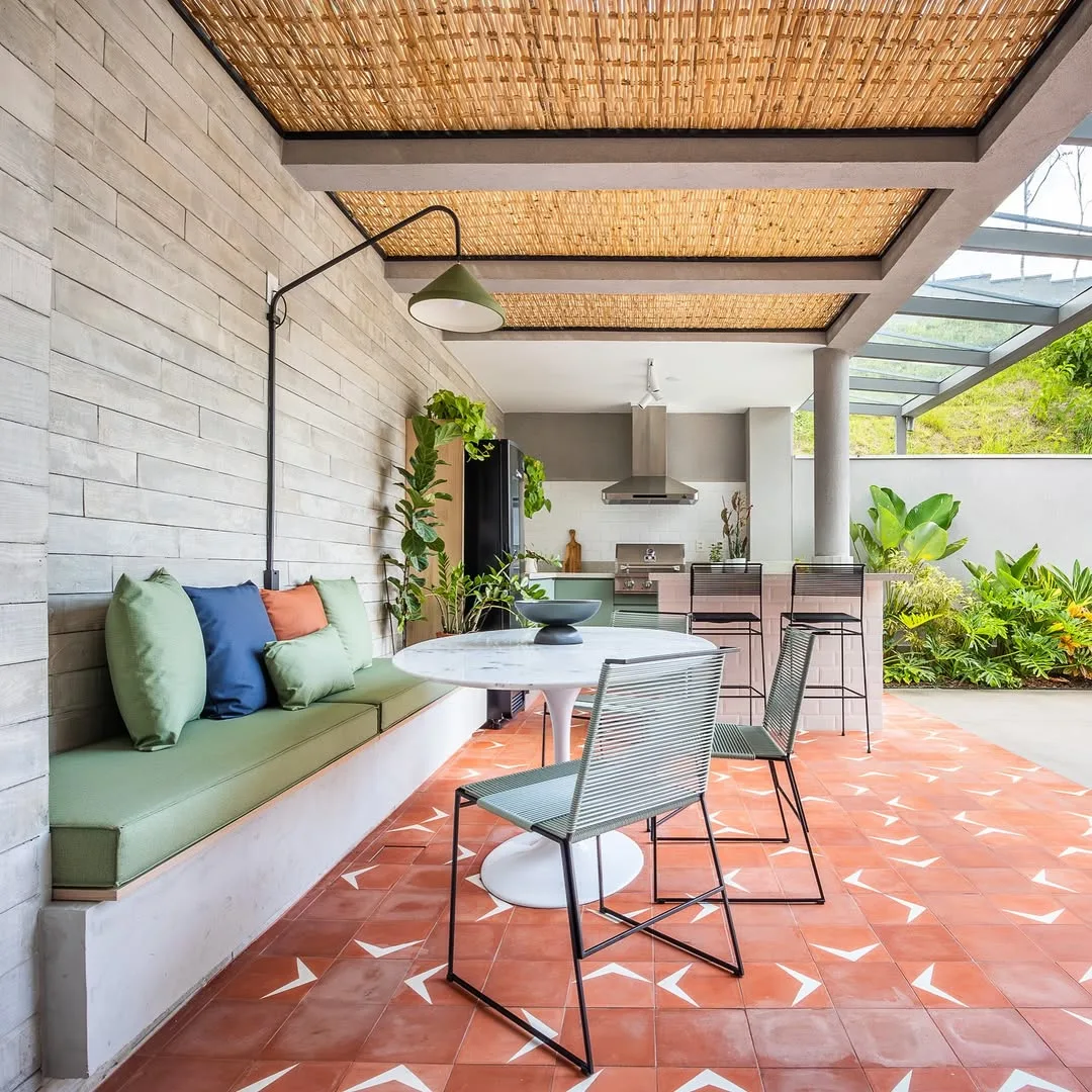 Varanda coberta com pergolado e forro de palha, sofá com almofadas verdes e azuis.