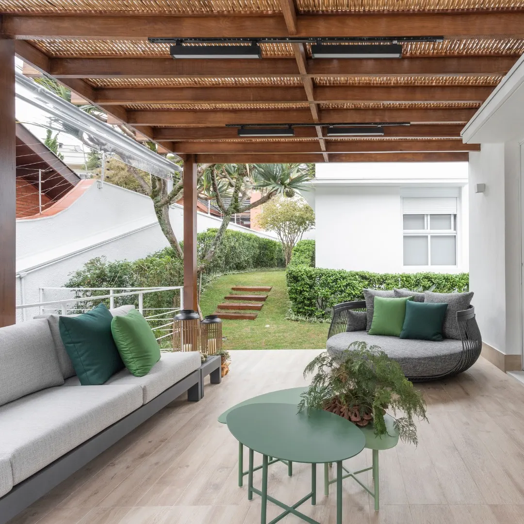 Varanda com pergolado de madeira, sofá neutro e almofadas coloridas de verde.
