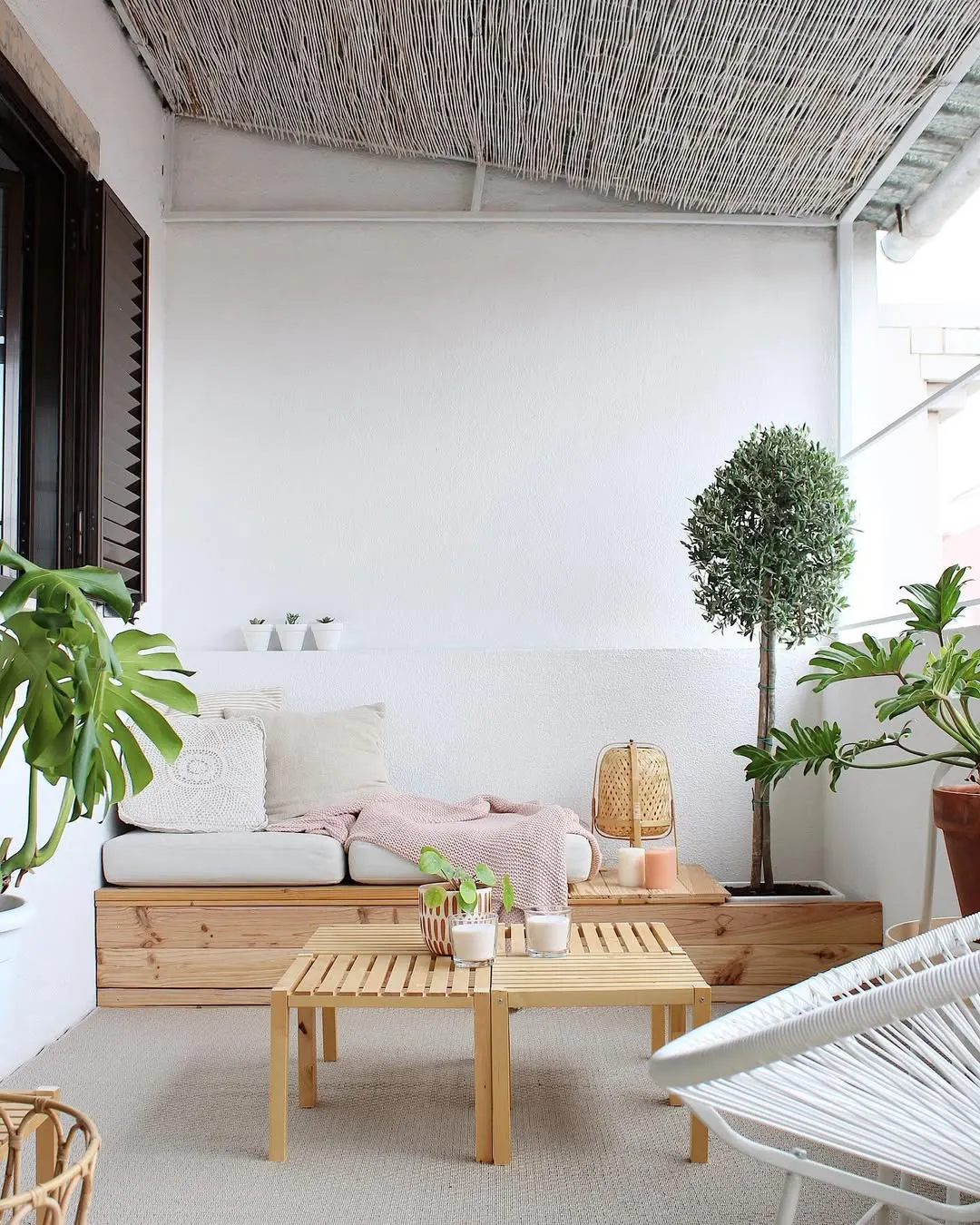 Ambiente sereno com mesa de centro de pallet, paredes brancas e sofá com almofada branca.