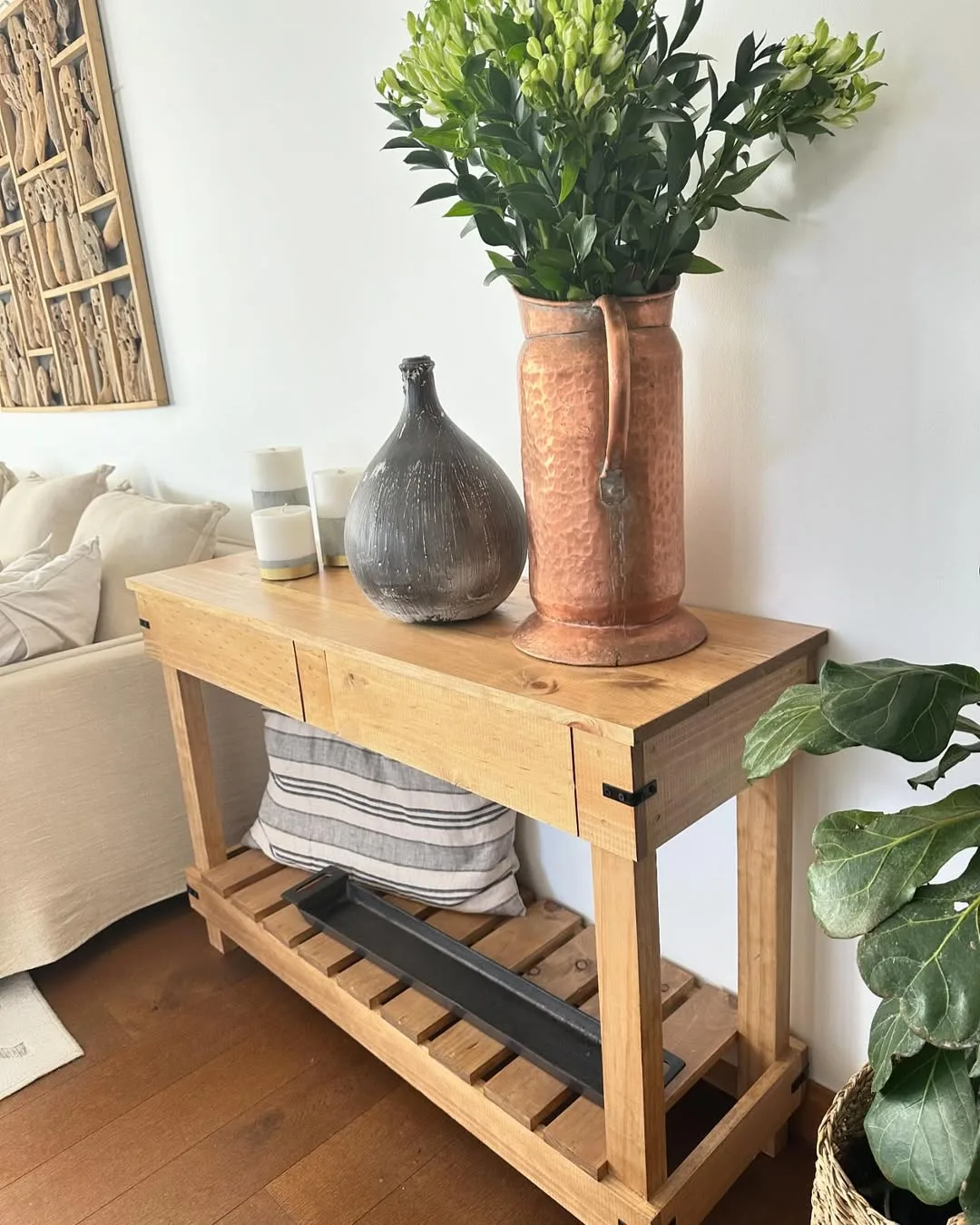 Aparador de pallet na sala de estar, vasos em cima e almofada embaixo.