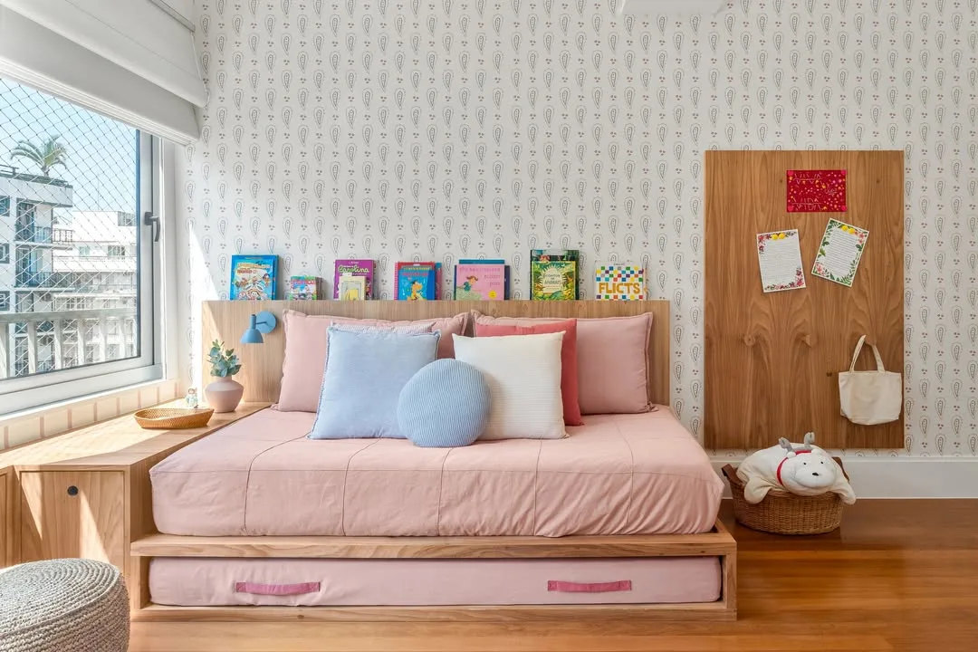 Quarto infantil com almofadas na cama baixa, papel de parede delicado.