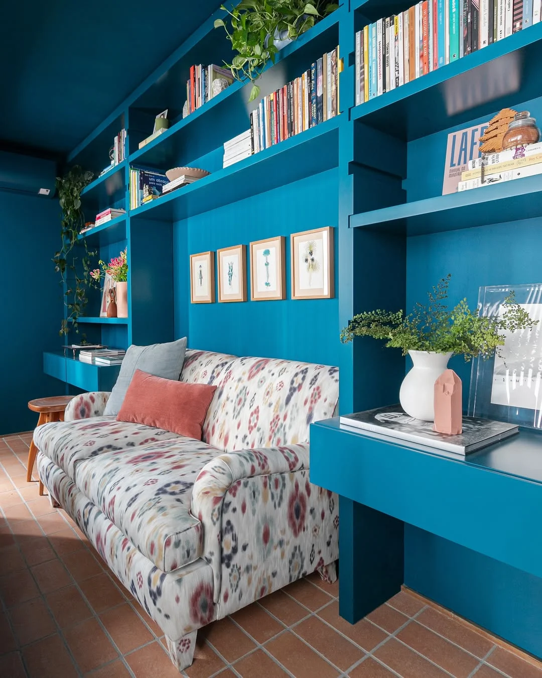 Decoração maximalista com sofá estampado e almofadas coloridas, parede de estante azul vibrante.