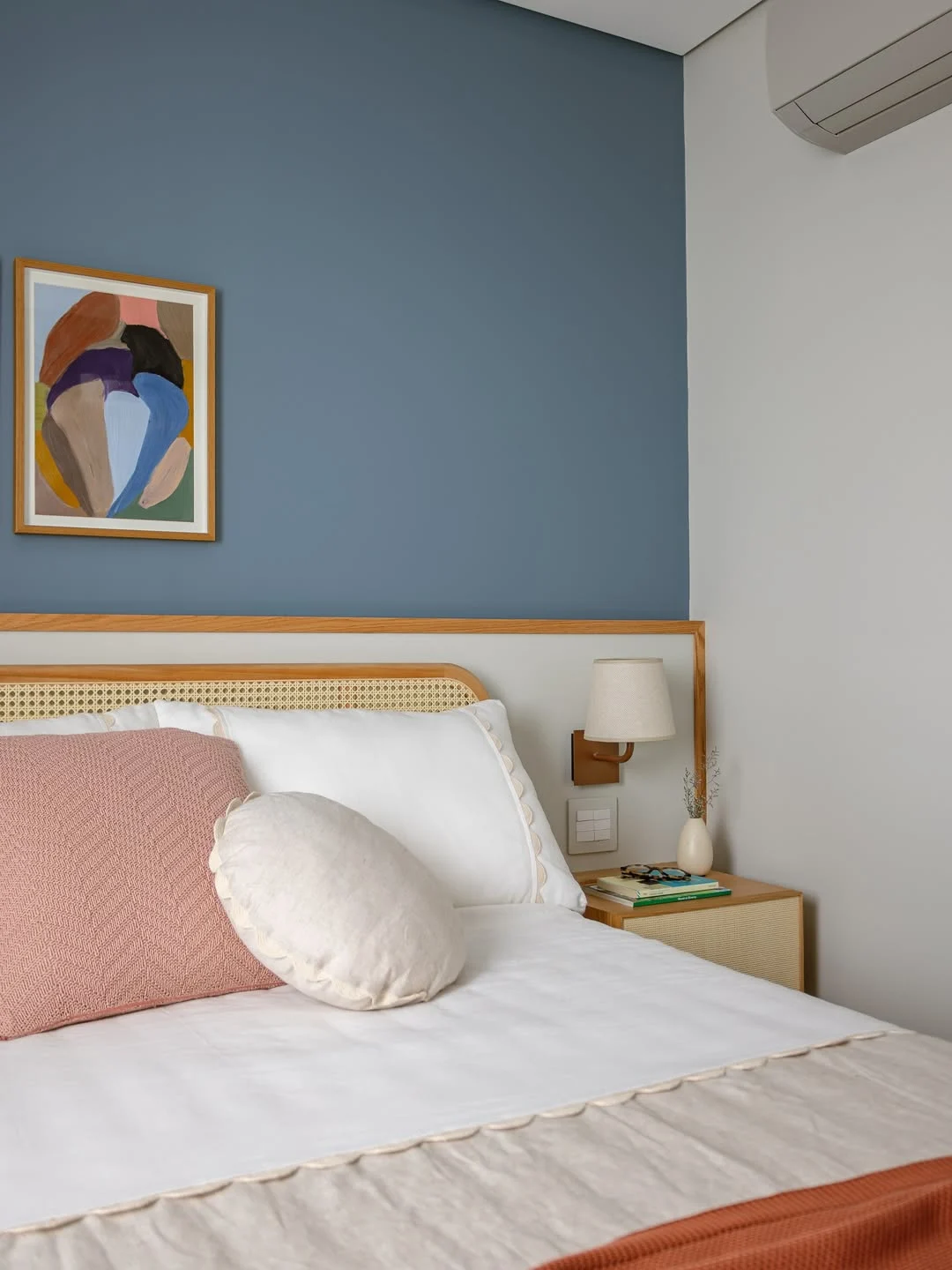 Quarto com almofada redonda, parede azul e cabeceira de palha italiana.