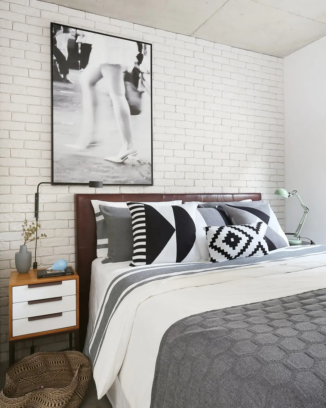 Quarto de adulto com quadro preto e branco, almofadas em preto e branco e colcha cinza.