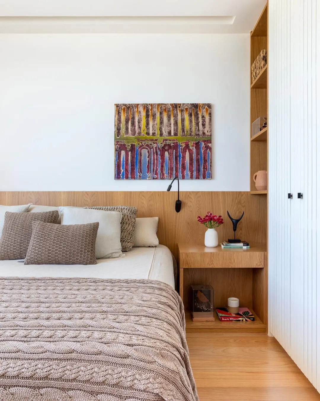 Quarto de adulto com quadro colorido na parede, almofadas na cama em tons de marrom.