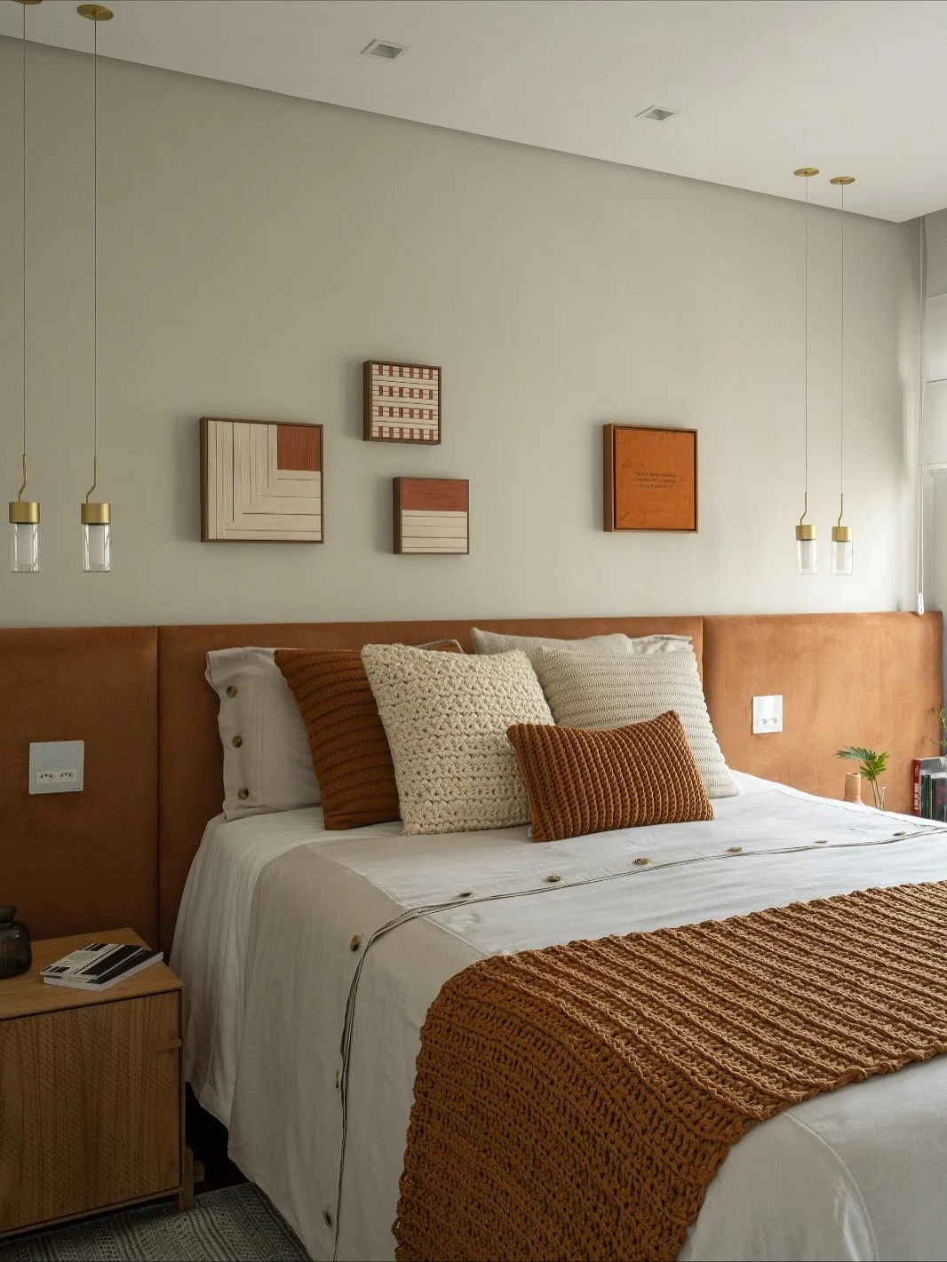 Quarto de adulto em tons terrosos, quadros na parede, cabeceira caramelo e manta marrom.