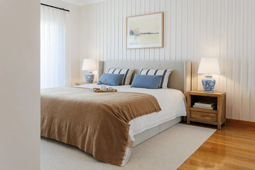 Quarto de adulto com almofadas tom sobre tom, manta marrom, papel de parede listrado.