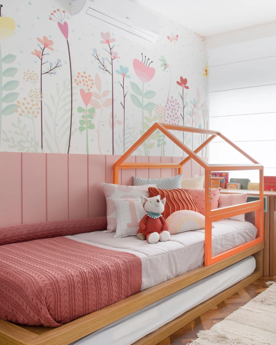 Quarto de criança feminino com estamapa de flores na parede, almofadsa variadas e bichinho de pelúcia.