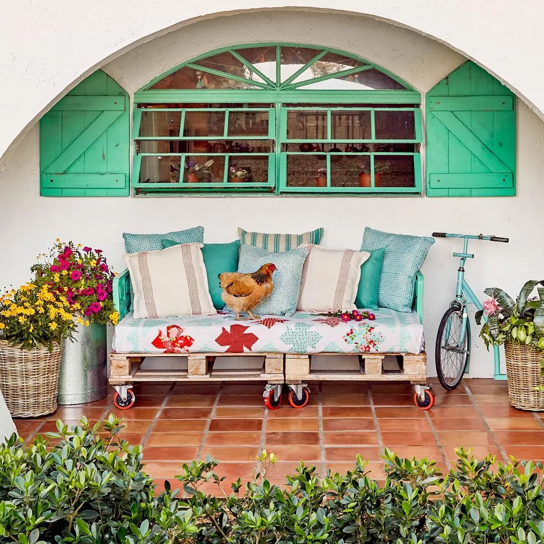 Pallet na área externa de asa, estampas nas almofadas, janela verde em arco e galinha.